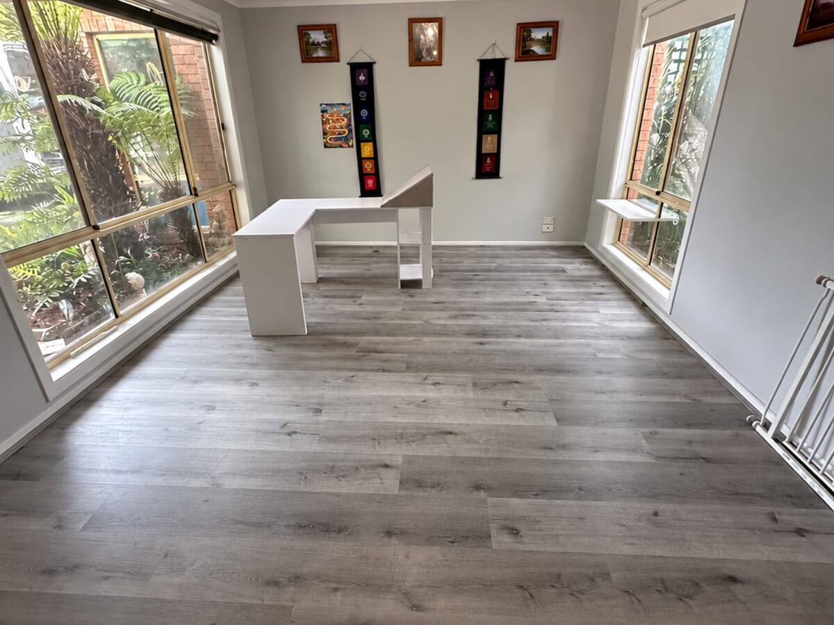 Dark Grey Oak 1005 flooring in a light-filled front room with windows on two walls and a white desk against the far wall.