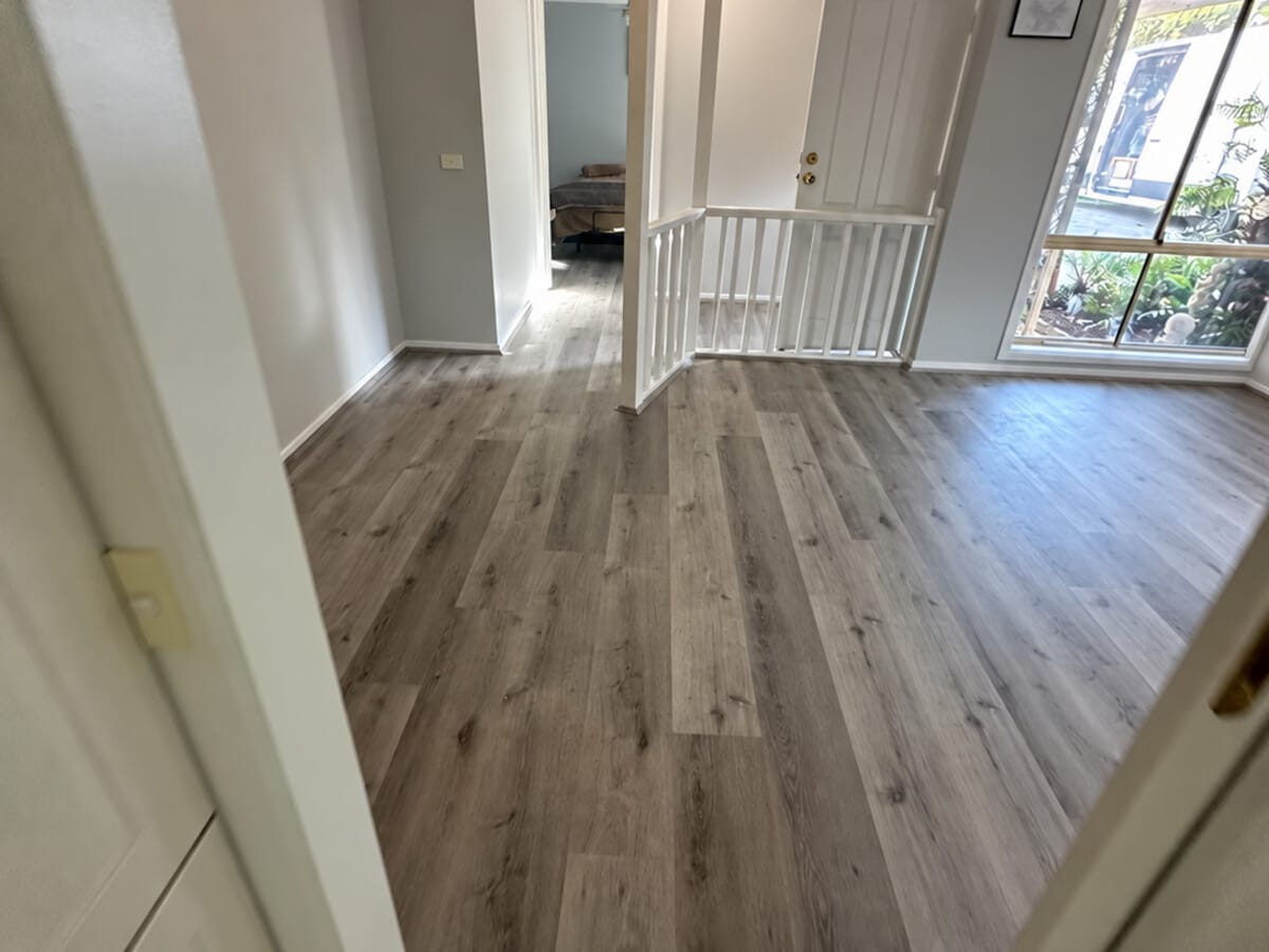 Dark Grey Oak 1005 flooring across an entry landing, with a white balustrade and the front door beyond.