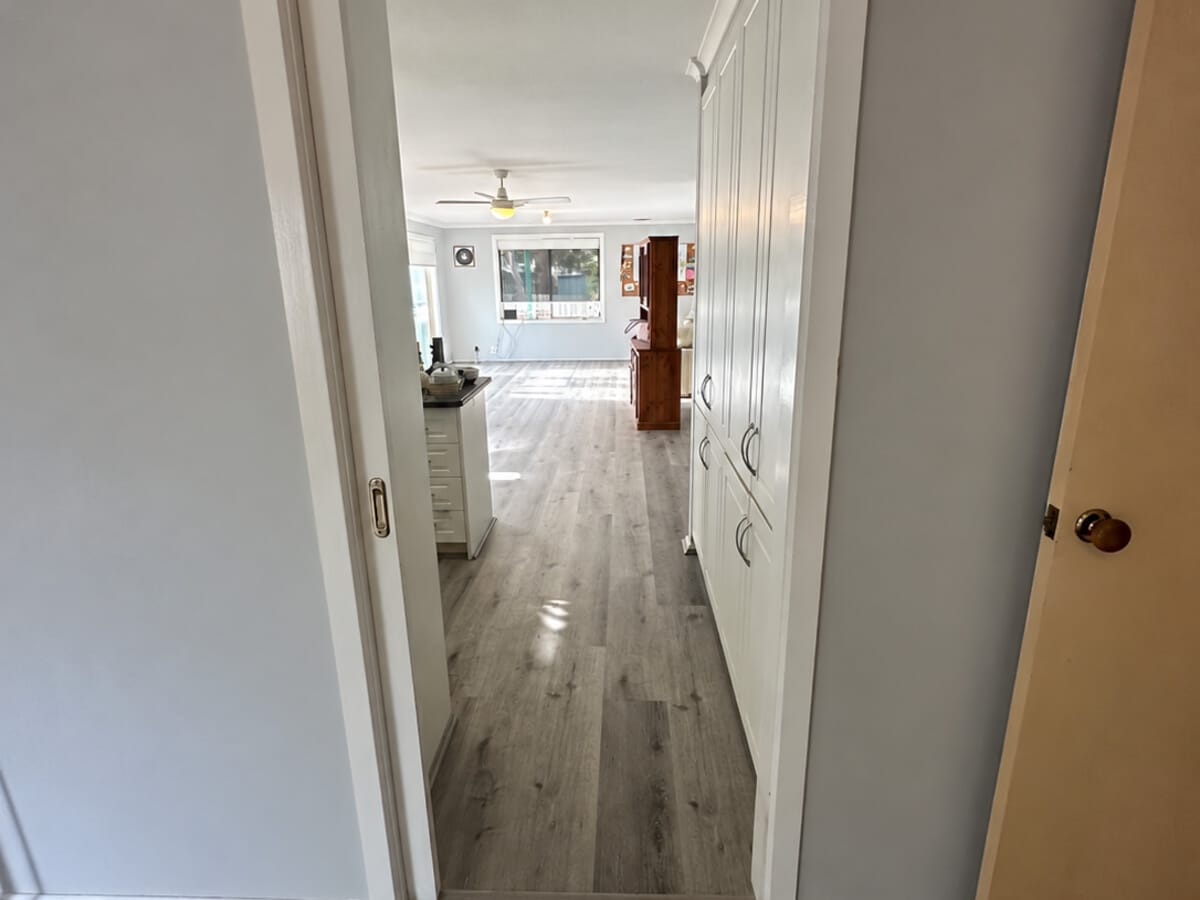 Dark Grey Oak 1005 planks down a hallway lined with white built-in cupboards, opening into a living room.