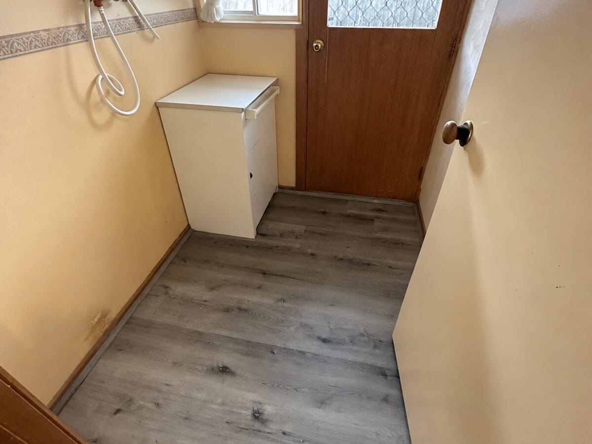 Dark Grey Oak 1005 planks continuing into a laundry and back entry, where the floor meets a timber rear door.