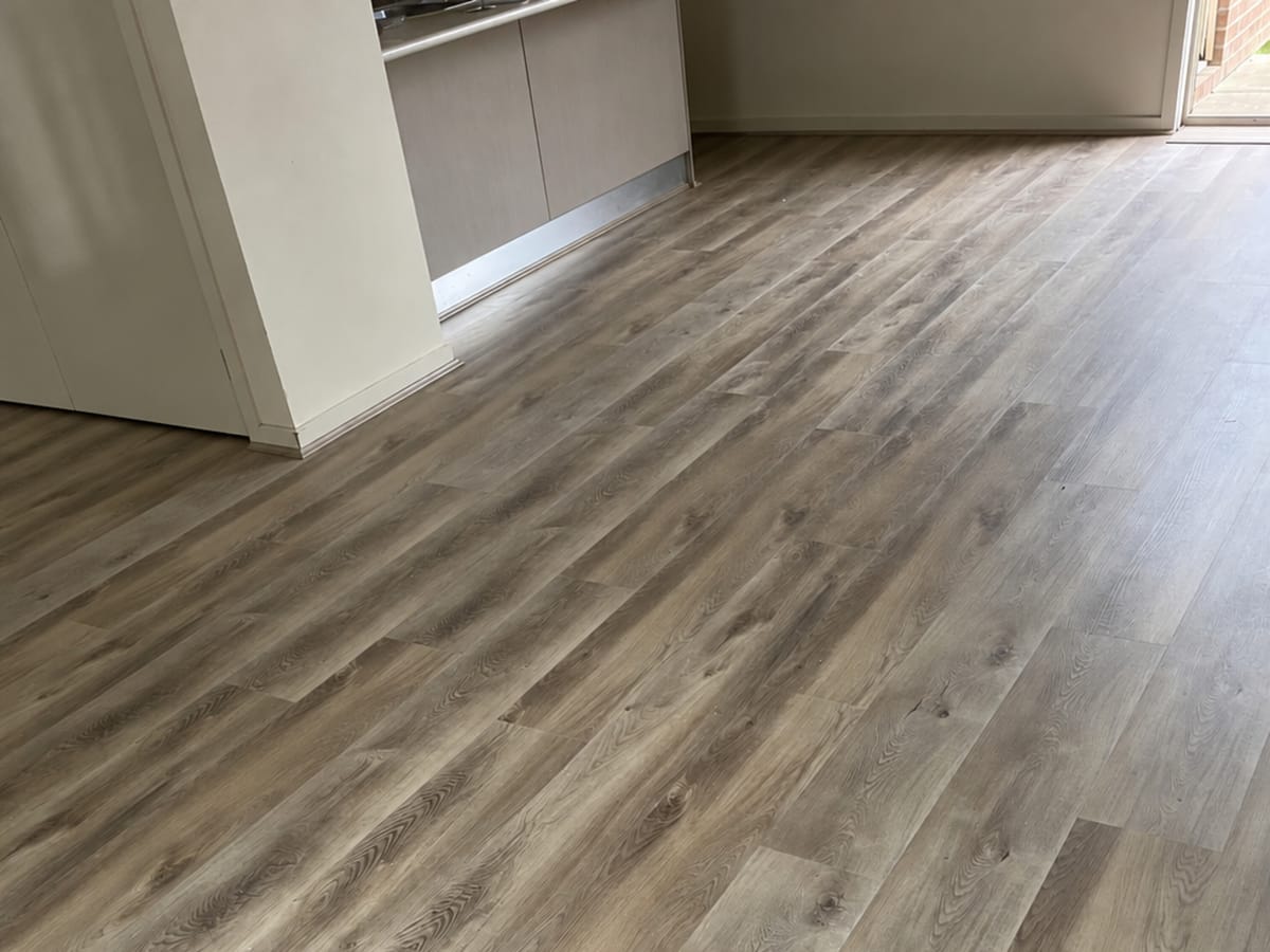 Coastal Oak 1009 hybrid planks running from a living area to a kitchen with pale cabinetry and a sliding door to the garden.