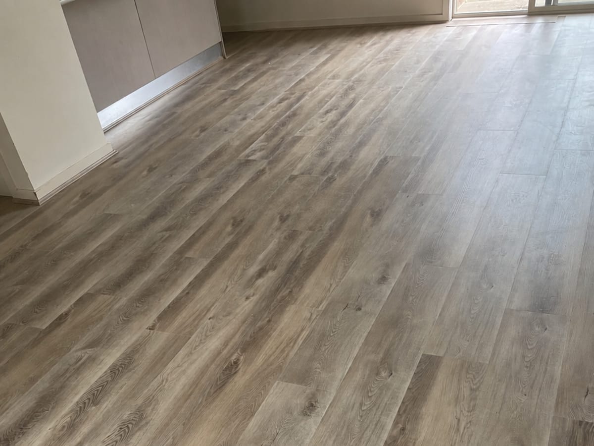 Coastal Oak 1009 flooring across an open living space, kitchen joinery at the left and glazed doors at the far end.