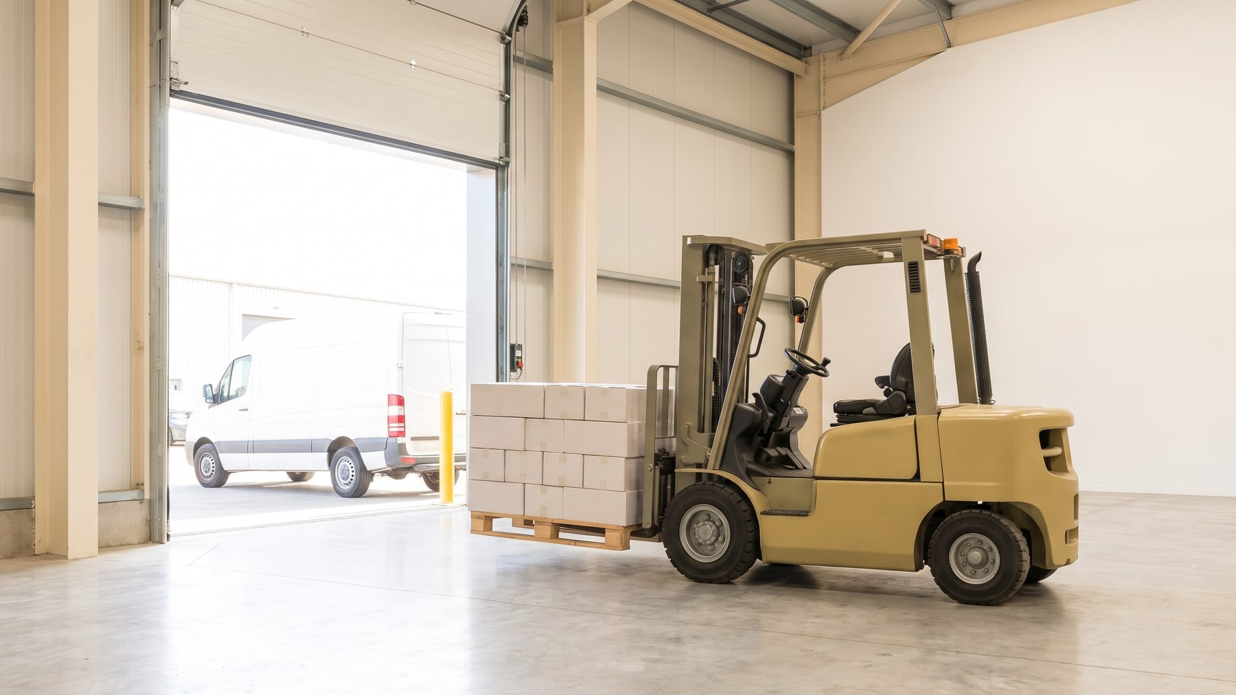 A forklift lifting a pallet of flooring cartons in a warehouse loading bay with the roller door open to daylight