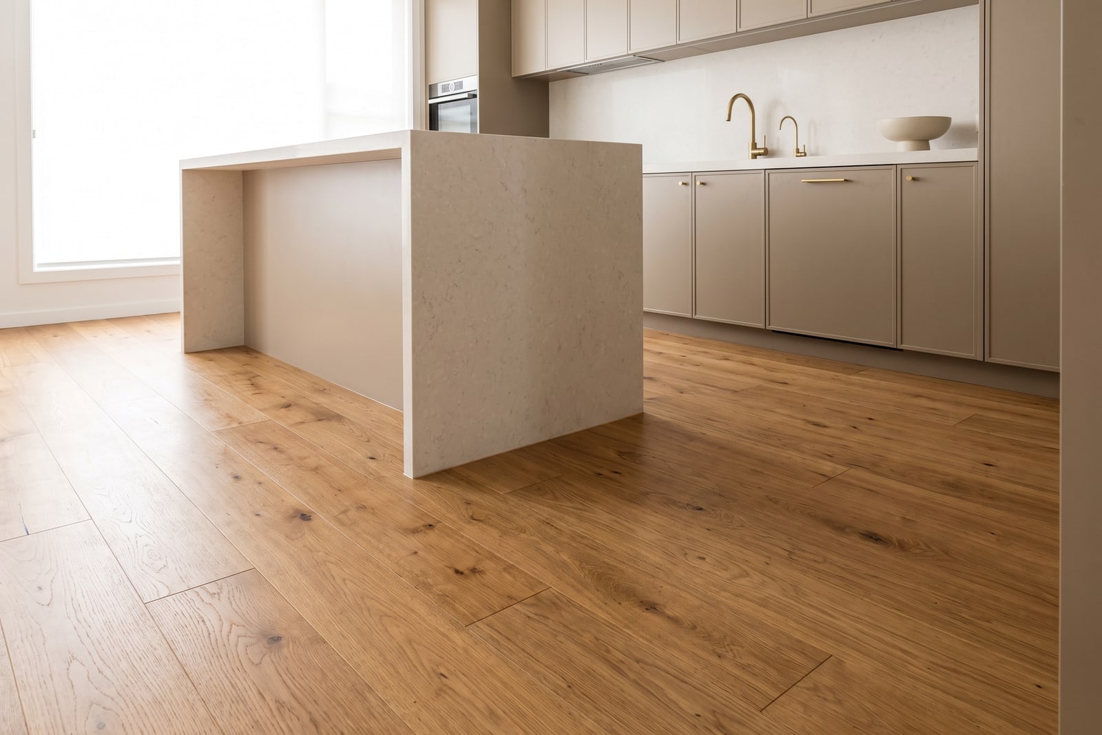 A modern kitchen with a stone-topped island and wide-plank timber-look flooring running unbroken beneath it