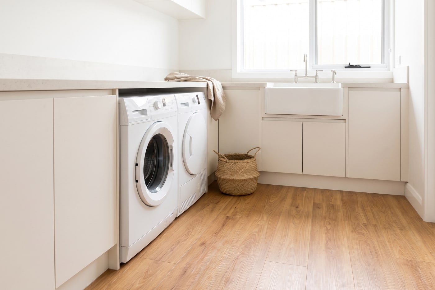 A modern laundry with a front-loading washing machine and timber-look flooring running unbroken across the floor