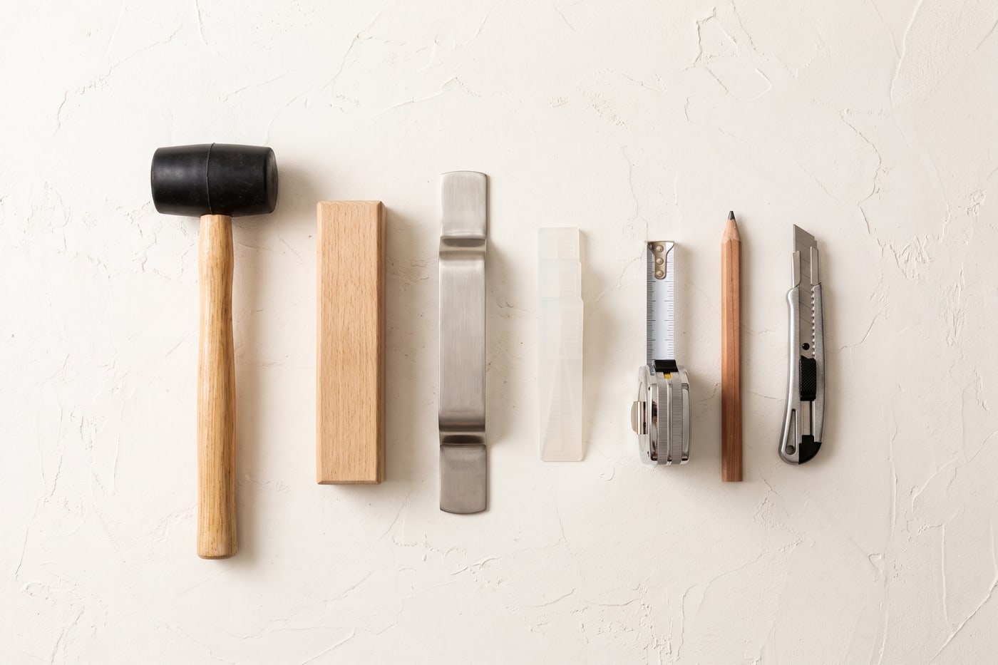 Flooring installation tools laid out in a row: rubber mallet, tapping block, pull bar, spacer wedges, tape measure and knife