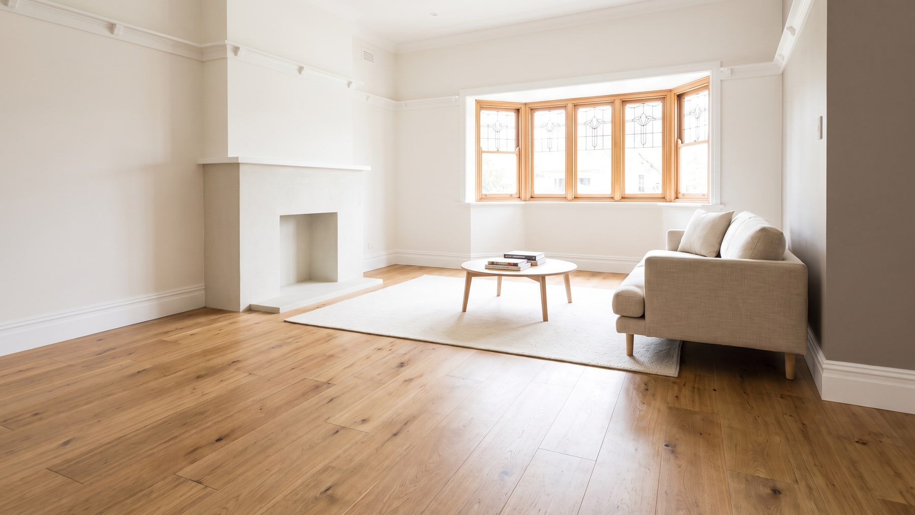 The living room of a renovated Californian bungalow with a leadlight bay window and wide-plank timber-look flooring