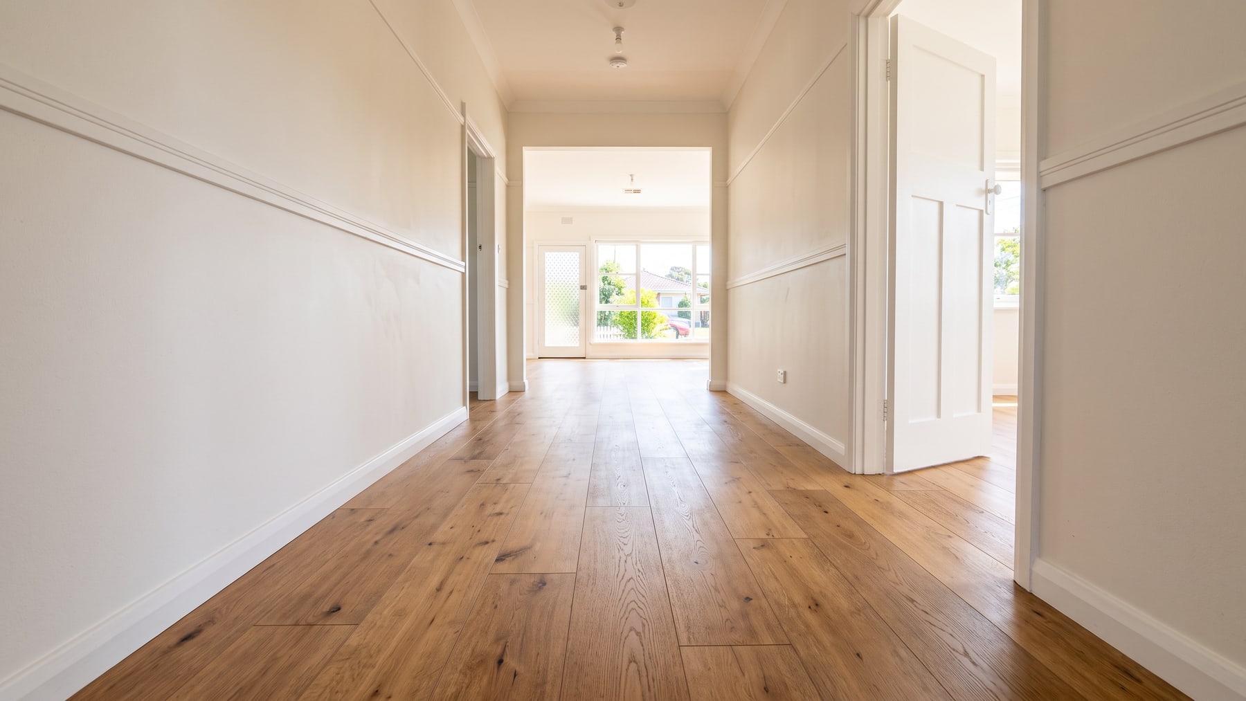 A hallway in a renovated post-war brick veneer house with newly laid wide-plank timber-look flooring running its length