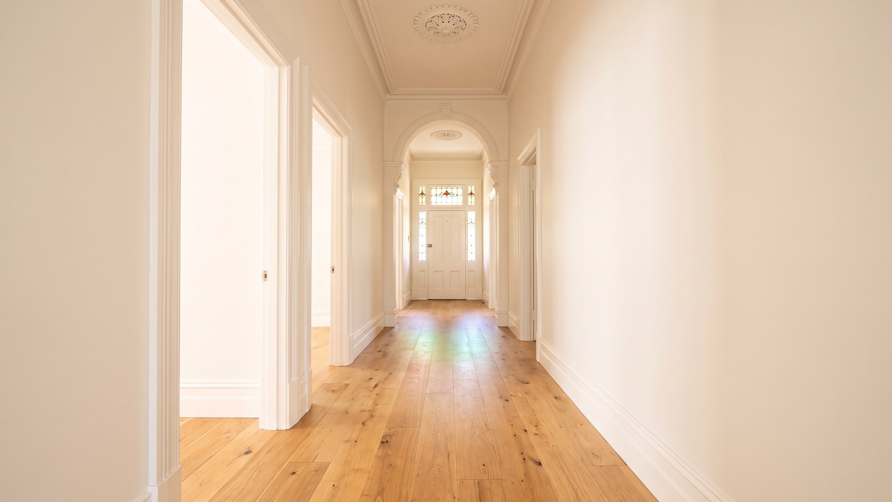 The hallway of a renovated Victorian terrace with a ceiling rose, leadlight over the door and wide-plank timber-look flooring