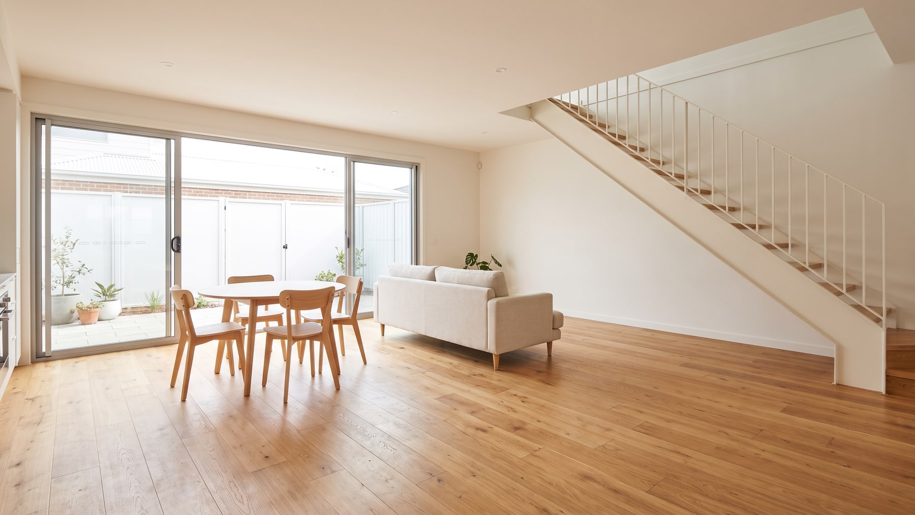 A newly completed townhouse living and dining space with wide-plank timber-look flooring running unbroken to a courtyard