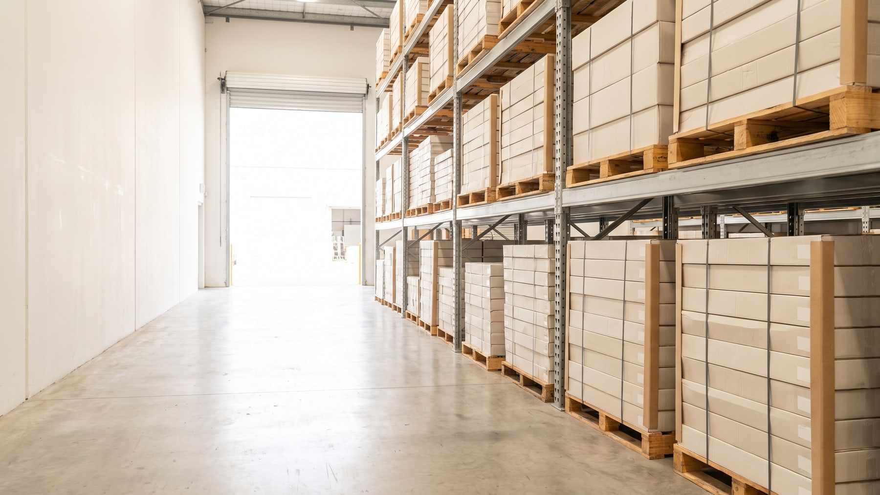 Pallet racking in a flooring warehouse, stacked with cartons on timber pallets beside an open roller door